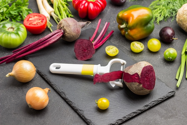 vegetable peeler and beets on cutting board tomatoes peppers and greens on table black background top view - Монастырская кухня: луковый суп с капустой, свекольные котлеты