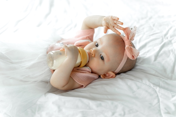 Особенности питания детей baby drinks milk from a bottle on a white bed - Особенности питания детей