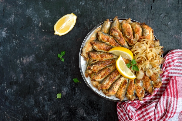 Жареная салака с прозрачным луком fried capelin sprats small fried fish on a plate on a black background top view - Жареная салака с прозрачным луком