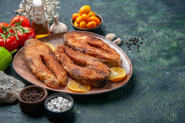 front close view of fried fishes and lemon slices on a brown plate spices tomatoes oil bottle on mix colors table with free space - Жареная рыба в соусе сациви