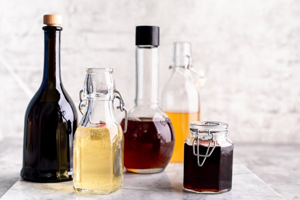 original glass bottles with different vinegar on a marble table against a table of a white brick wall copy space horizontal - Жареный корень лопуха