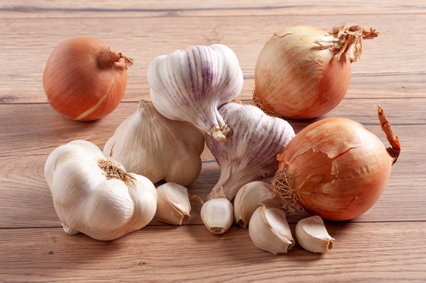 pile of whole onions and garlic bulbs and cloves on a wooden table - Острый рыбный суп с томатом