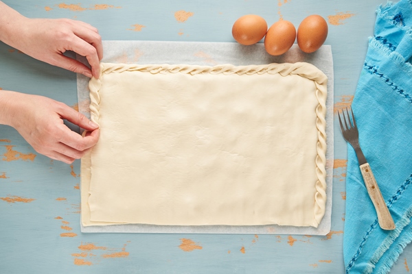 person makes an edge to the dough of the galician raw empanada filled with tuna - Спанакопита