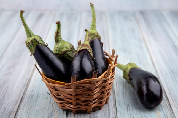 side view of eggplants in basket and on wooden background - Баклажаны с чесноком "Шашлычные"