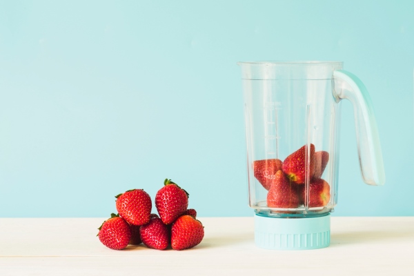 milk bottle near strawberry in blender on wooden table - Холодный фруктовый суп