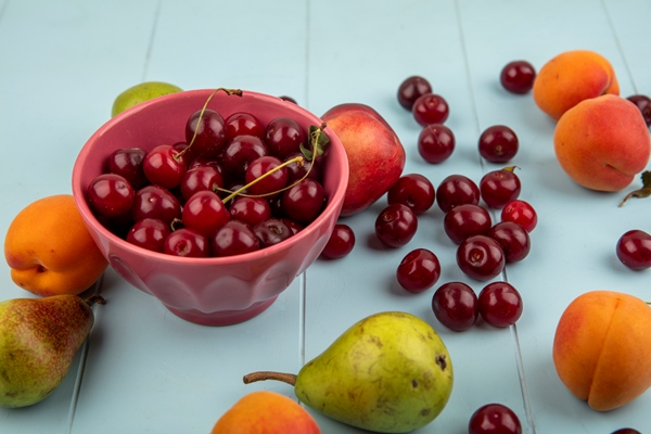 side view of cherries in bowl and pattern of peach apricot pear cherry on blue background - Холодный фруктовый суп