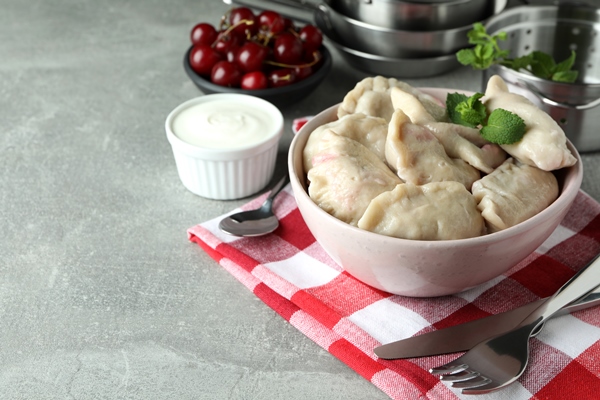 concept of tasty food with pierogi with cherry on gray textured table - Вареники с вишней