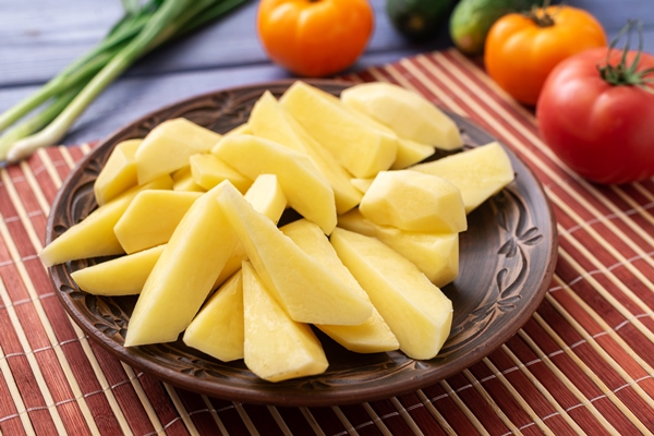 tubers of raw peeled cut potatoes on a plate on the kitchen table with vegetables - Турецкая запеканка с кебабом