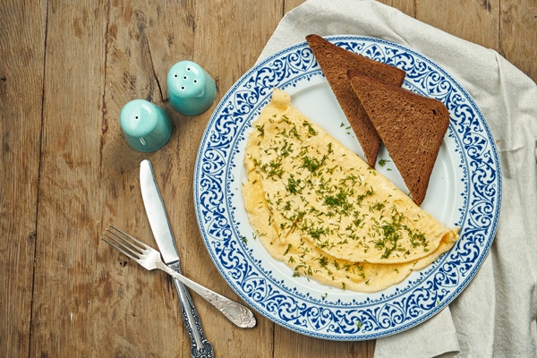 appetizing breakfast omelet with greens and rye toast on a ceramic plate on a wooden surface - Омлет "Туристический"