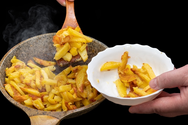 hand of the chef putting delicious crispy golden hot fried potato wedges into a white plate with a wooden spatula close up delicious homemade food a traditional dish - Жареный картофель с луком