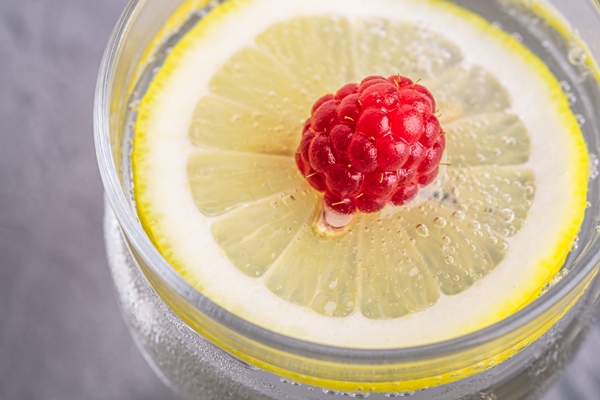 fresh cold sparkling water drink with lemon raspberry fruits in glass on stone - width=
