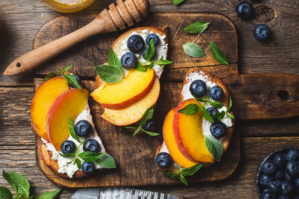 white bread sandwich with peaches blueberries on a wooden board - width=