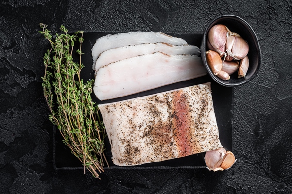 sliced salty lard with garlic black pepper marble board black background top view - Сало солёное (сухой посол)