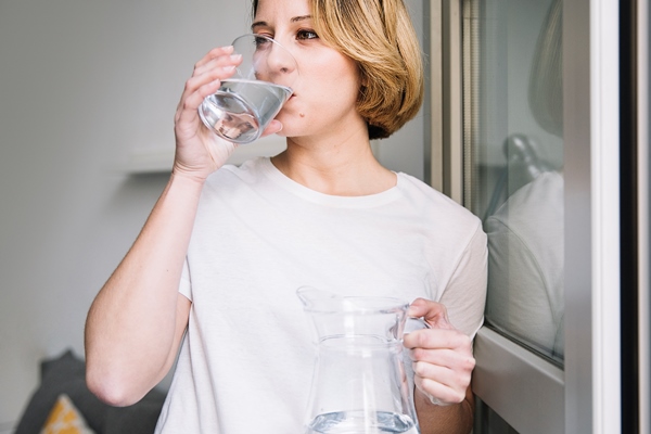 Сколько воды нужно выпивать в день woman drinking water near window - Сколько воды нужно выпивать в день