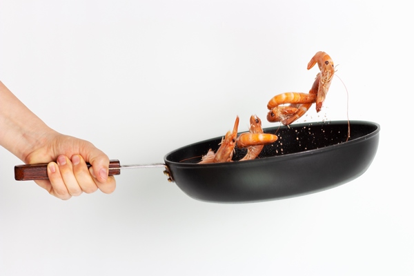 Обжаривание woman s hand holds frying pan frys shrimp white surface - Обжаривание