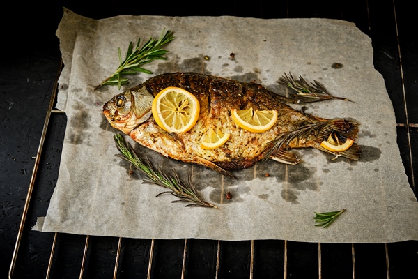 baked fish cooked parchment paper with spices lemon rosemary barbecue grill dark background - Карп на мангале