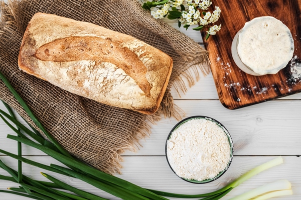 zakvaska dla prigotovlenia hleba muki i svezeispecennogo hleba na belom derevannom stole - Крестьянский хлеб с отрубями